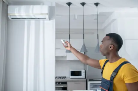 A technician uses a remote control to test a wall-mounted air conditioner.