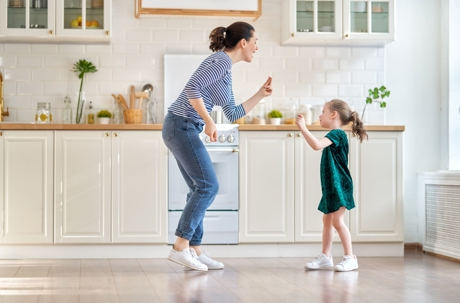 A mother and her young daughter playfully dance together in the kitchen