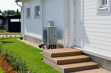 An outdoor heat pump unit is installed next to the wooden steps of a white house.