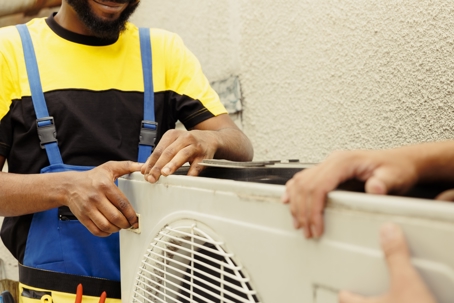 Two technicians work together to service an outdoor air conditioning unit.