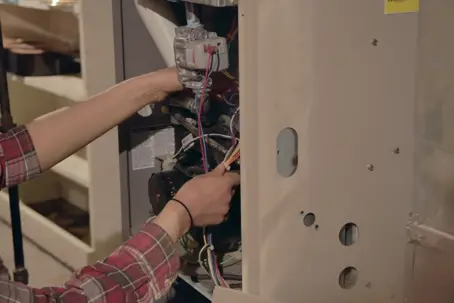 A person works on the internal wiring of an open furnace.