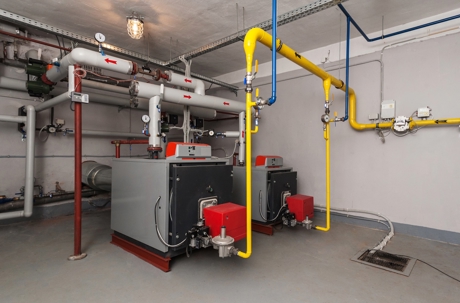 Two industrial boilers connected to yellow gas lines sit in a mechanical room.