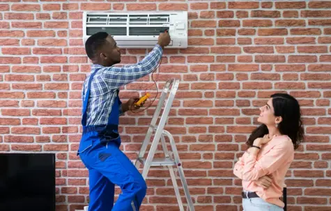 A technician is repairing the AC unit while the owner is watching