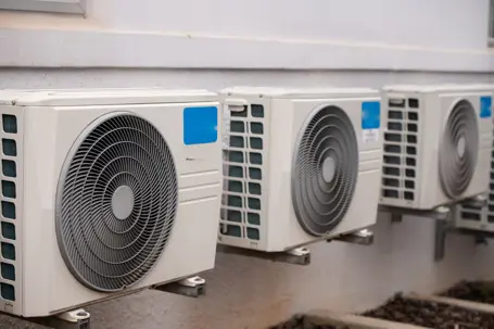 A row of outdoor air conditioning units is mounted along the exterior wall of a building.
