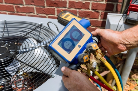 A technician uses a digital manifold gauge to check pressure on an outdoor air conditioning unit.