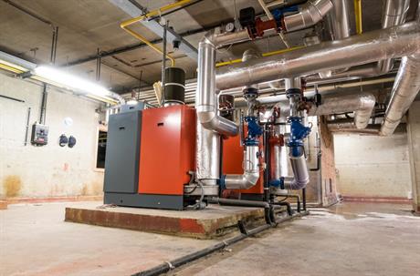 Large industrial boilers and insulated piping fill a concrete mechanical room.