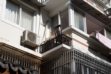 A wooden chair sits on a small apartment balcony next to an air conditioning unit.