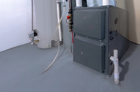 A dark gray furnace and a white water heater stand in a clean utility room.