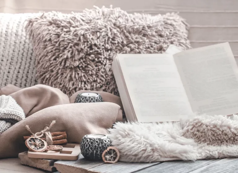 6 REASONS WHY GETTING A MAINTENANCE PLAN IS GOOD CHOICE FOR YOU 2 An open book rests among soft blankets, textured pillows, small candles, and cinnamon sticks in a cozy setting.