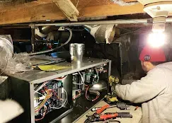 Technician working on HVAC system in a dimly lit basement.